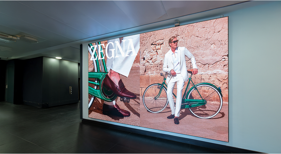 Advertising billboard in VIP Private Jet Terminal showing a man in white suit standing next to a green bicycle and close-up of brown shoes on a green chair
