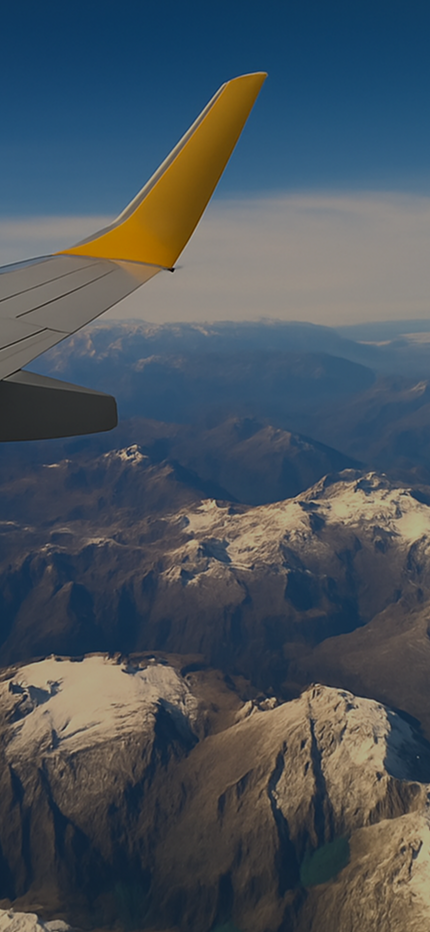 View of airplane wing with yellow tip flying over snow-covered mountains under a clear blue sky